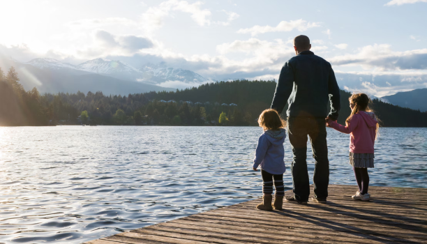 Un père et ses deux enfants se tiennent la main debout sur un quai.