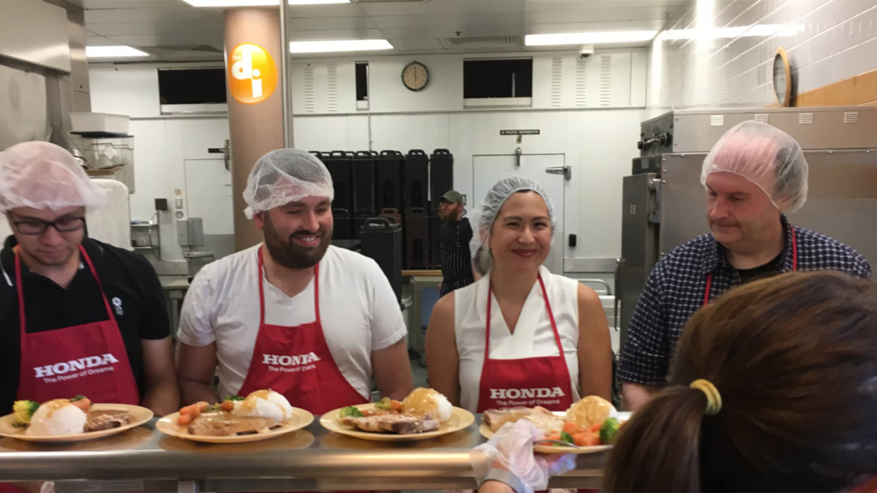 Des employés de Honda en tablier rouge travaillant dans une cuisine collective.