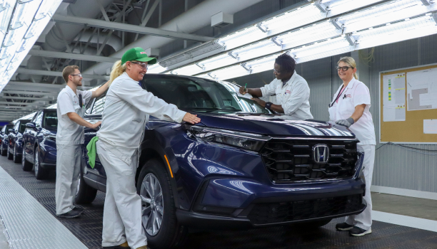 Un groupe d’employés Honda en sarrau blanc sur la chaîne de production et souriants.
